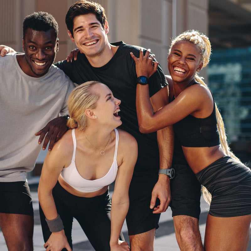 Four people in athletic wear posing together outdoors with a cityscape background