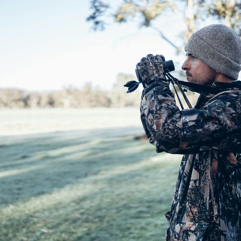 Person in camouflage clothing using binoculars in a natural setting