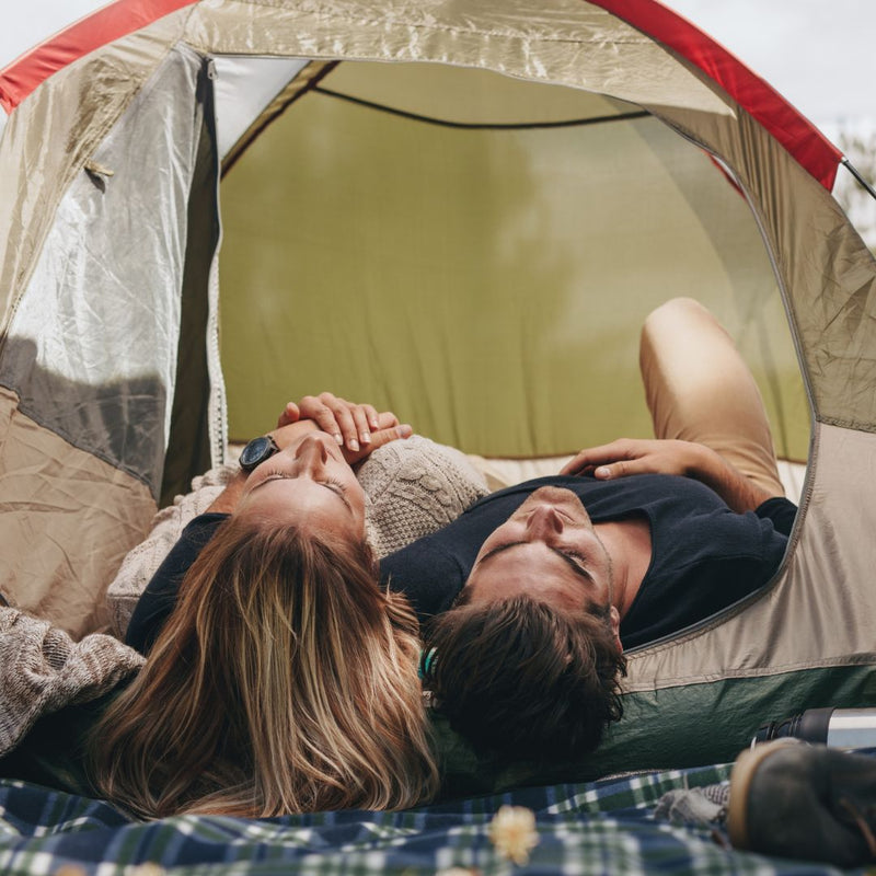 Two people lying inside a tent, enjoying a moment together.