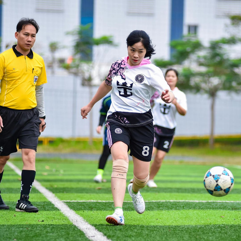 Woman playing soccer on a field with a referee and other players in the background.